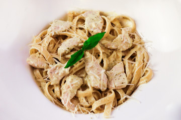 Italianate pasta with basil leaves and Parmesan cheese in a white plate on a wooden background