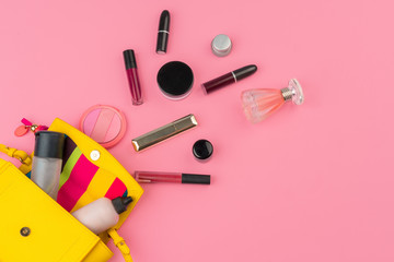 Female small handbag full of cosmetic products on bright pink background