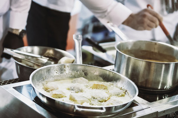 Group of professional chefs work in a restaurant or hotel and prepare a dish of fried fish (reduced tone)