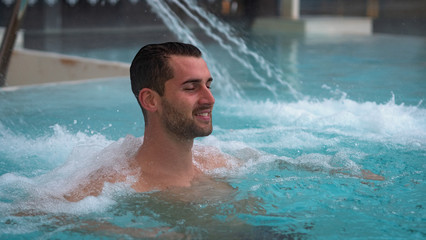 Portrait of an young man is enjoying and having relax in a whirlpool bath tube in a luxury wellness...