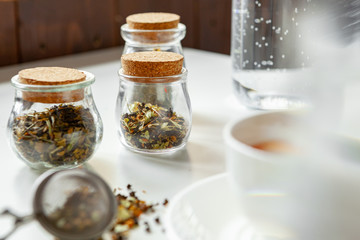 Glass jars with dry tea leaves close up on white table