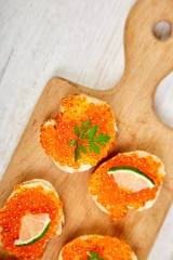 Salmon red caviar in bowl and Sandwiches with on wooden cutting board on white background copy space.