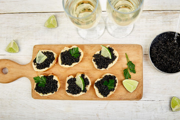 Sandwiches with black caviar. Sturgeon black caviar in wooden bowl, sandwiches and champagne on white background copy space. Top view..