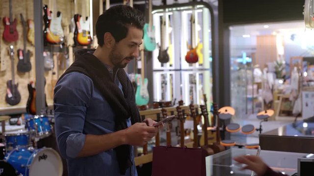 An upwardly mobile Middle Eastern man using a mobile phone to scan the QR Code for verification, authentication and secure payment transaction at the point of sale terminal in a retail store