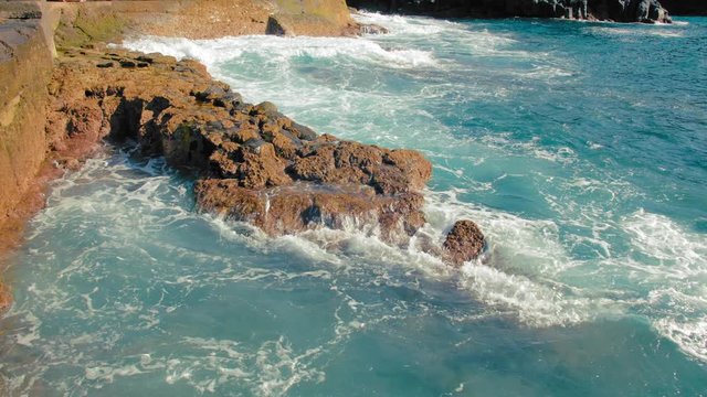 Turquoise waves of the ocean beat against the yellow stones of the shore. Massive white foam and spray form. concept of ebbs in the oceans.