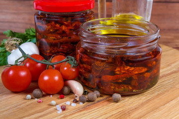 Dried tomatoes in olive oil in jars among ingredients closeup