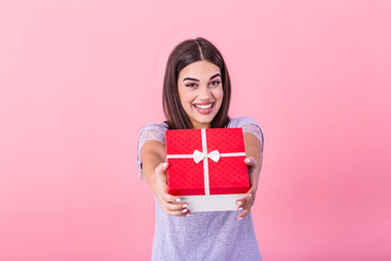 Happy brunette woman in casual holding gift box and looking at the camera while enjoys over pink...