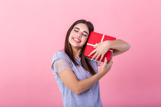 Image of happy cheerful young girl isolated over pink wall background holding surprise box gift. Excited young casual brunette woman holding present box