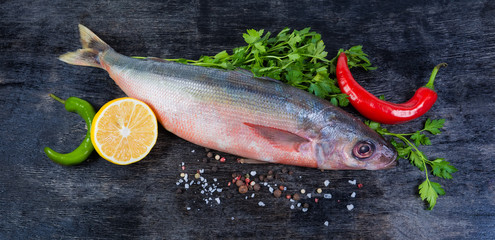 Carcass of uncooked Redbait fish and spices on black surface