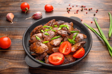 Homemade chicken liver fried with soy sauce, tomatoes, onions and spices on wood background. Close up