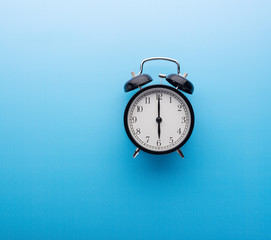 Alarm clock on blue background top view. Six o'clock.