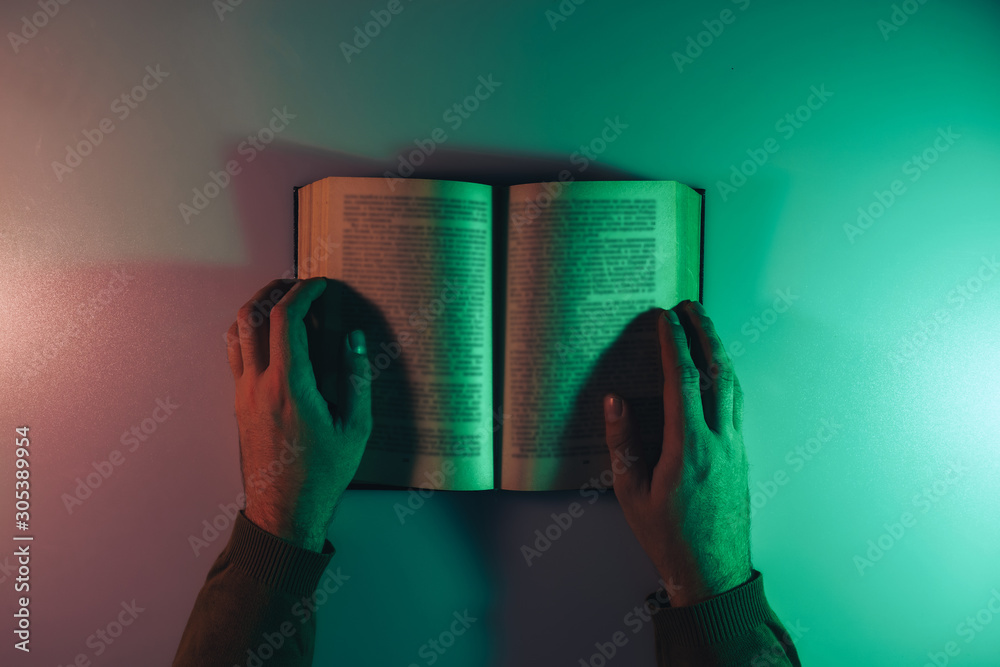 Poster beautiful man reading book in the color light on a table and night background.
