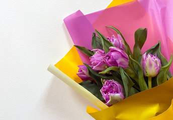 Bouquet of purple tulips in multi-colored paper on a light background