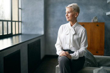 Indoor image of confident beautiful middle aged female psycologist wearing white blouse sitting on...