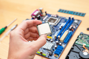 Computer processor in hand. Motherboard is ready for installation in background. Beside is hard...