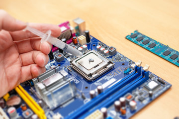 Applying thermal paste to a computer processor. Processor installation concept and cooling solution. Blue motherboard and RAM memory stick beside. Close-up.