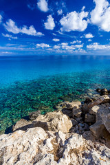 Sea coast with clear turquoise water and sharp stones, blue sky with clouds.