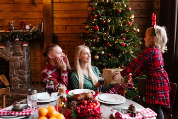 Child sitting at the holiday table, gives parents Christmas gifts on the background of the Christmas tree