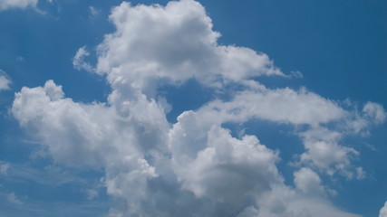 Ant's eye view of fat white clouds moving in strong wind with blue sky background.