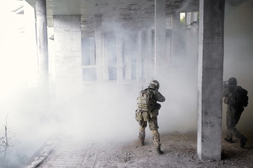 Two military soldiers storming a destroyed building with terrorists in a smoke filled room from a fire