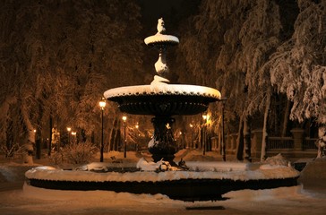 Antique cast-iron fountain, covered with snow. Winter City Park under the night illumination in New Year eve