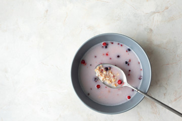 Gray bowl with oat, berry and milk at breakfast on marble table background with copy space. Top view, horizontal format
