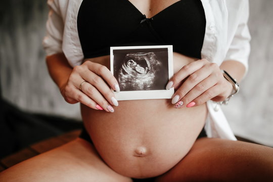 Pregnant woman in lingerie holding an ultrasound picture with her baby in front of her