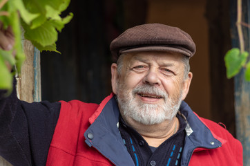 Nice positive portrait of Ukrainian bearded smiling senior peasant against old barn entry .