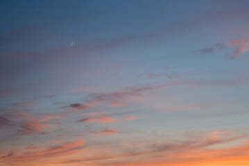 An orange sunset sky with the moon and clouds