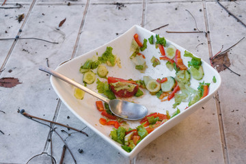 Finished eating. White bowl with spoon and leftover vegetable salad.  White plate on white table.