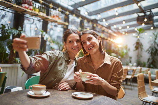 Portrait of two women smiling at smartphone camera while taking selfie photo in outdoor cafe