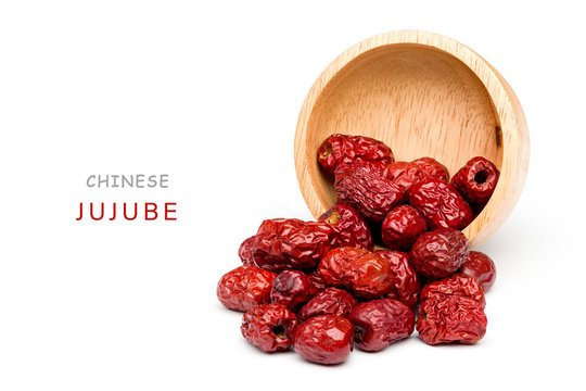 Bright red Chinese jujube was poured out of a wooden cup spread on a white background.