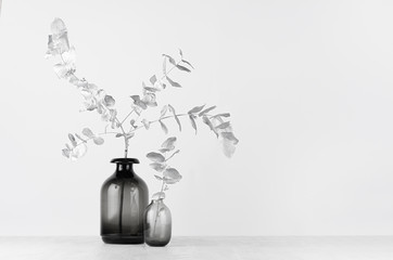 Elegant black and white home decor - black glass vase decorated silver leaves on light white wood table.