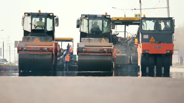 Front view of asphalt-placing machines and workers. Road construction process.