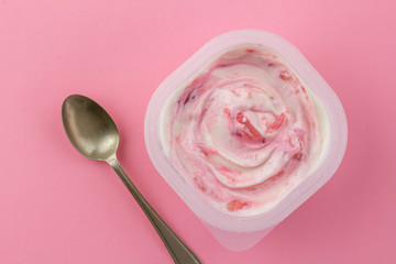 Strawberrry pink yogurt in white plastic cup with spoon isolated on bright pink background