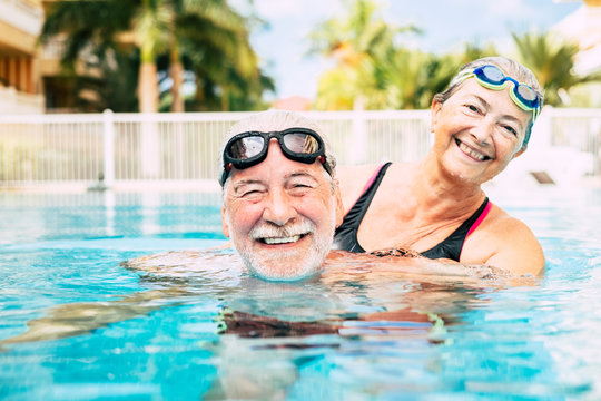 couple of two seniors hugged in the water of swimming pool - active man and woman doing exercise together at the pool - hugged with love - Powered by Adobe