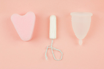 Close up of menstrual cup, tampon and sponge on pink
