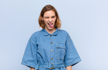 young blonde woman with cheerful, carefree, rebellious attitude, joking and sticking tongue out,...