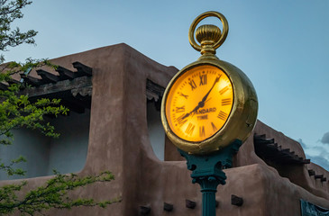 Naklejka premium Złoty post zegar na świeżym powietrzu na placu Santa Fe, tradycyjnej architekturze i błękitne niebo na tle zachodu słońca, Nowy Meksyk, USA.