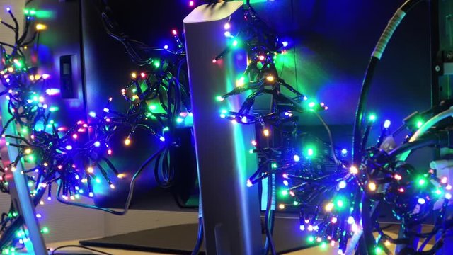Panning over blurry Christmas Led illumination placed at the back side of office computer and two monitors. Decoration lights in darker room before the Christmas when office staff leave for holidays