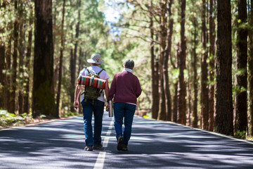 Travel lifestyle for old senior couple walking together in the middle of the road with high trees...