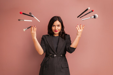 Studio photo of makeup artist woman smiling and throws up brushes and tools over a beige...