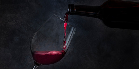 Wine poured into a glass from a bottle, panoramic shot on a dark background with copyspace