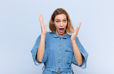 young blonde woman looking shocked and astonished, with jaw dropped in surprise when realizing...