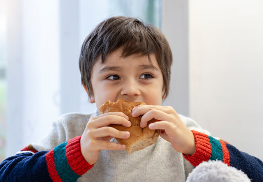 Preschool kid boy eating bacon sandwich sitting in nursery cafe, Cute happy boy eating bacon roll sitting in the restaurant. Healthy child eating delicious homemade food.