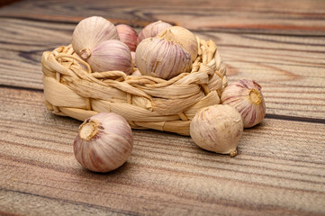 A few heads of young garlic in a wicker basket on a wooden background. Autumn harvest. Modern agriculture. Close up.
