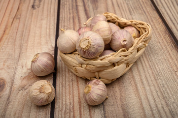 A few heads of young garlic in a wicker basket on a wooden background. Autumn harvest. Modern agriculture. Close up.