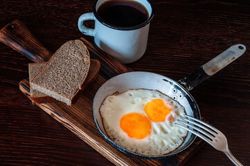 Fried scrambled eggs in vintage pan, with bread, old fork, metal mug with tea, top view