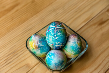 Obraz na płótnie Canvas Easter decoration - blue, colorful painted eggs with gemstones in a glass bowl on a glass table