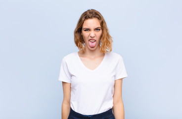 young blonde woman feeling disgusted and irritated, sticking tongue out, disliking something nasty...